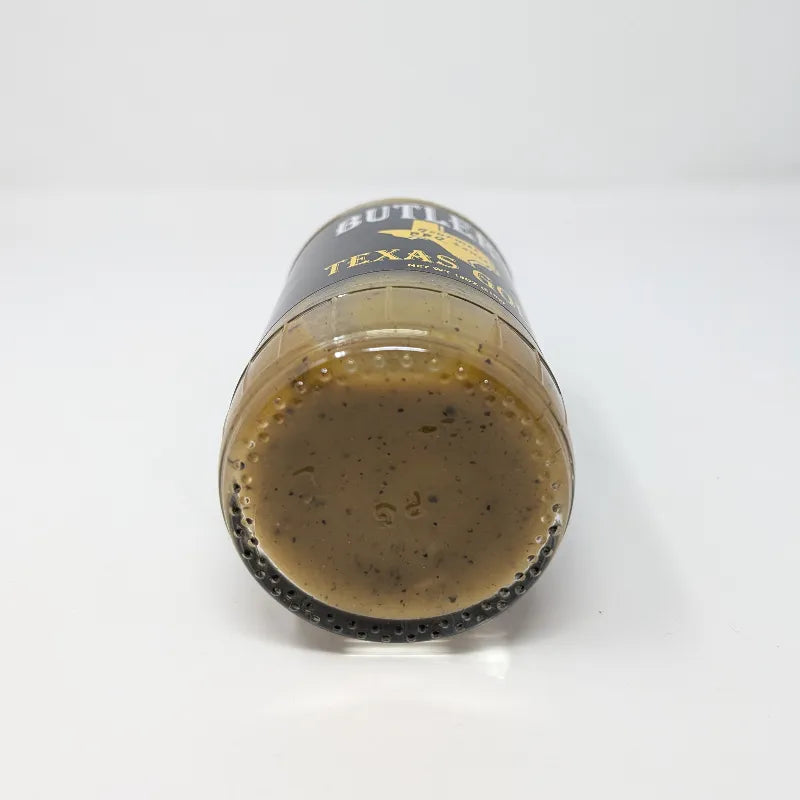 Bottom view of a bottle of Butler's Texas Gold Gourmet BBQ Sauce on a plain white background. The bottle is filled with a golden-brown sauce and features a black label with white and yellow text.