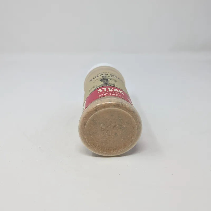 Bottom view of a 6 oz plastic bottle of Signature Nolan Ryan Beef Steak Seasoning with a white cap and a beige label featuring a Nolan Ryan portrait and 'STEAK' on a red band.