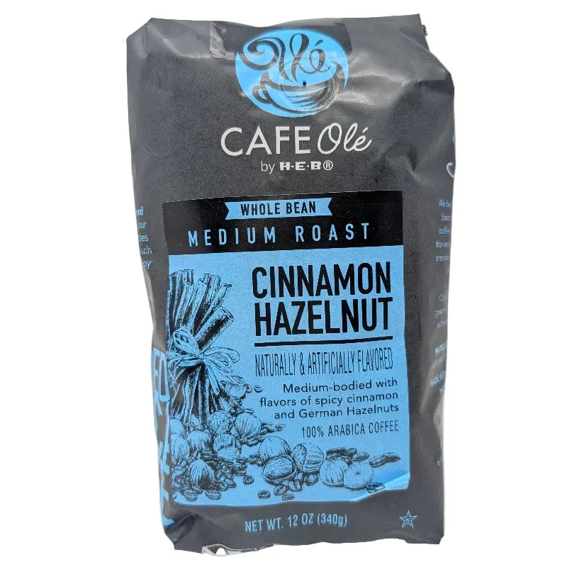 Front view of a dark gray and blue 12 ounce bag of Cafe Ole Cinnamon Hazelnut whole bean coffee on a white background.