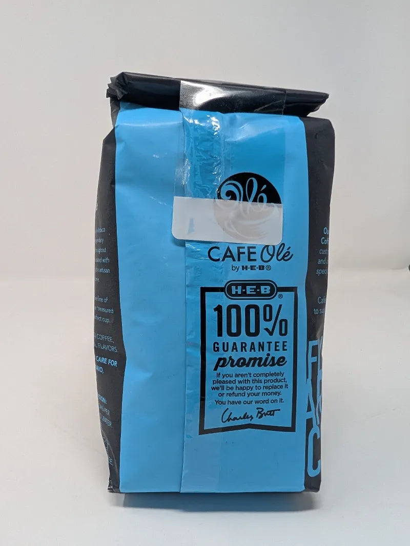Rear view of a dark gray and blue 12 ounce bag of Cafe Ole Cinnamon Hazelnut whole bean coffee on a white background.