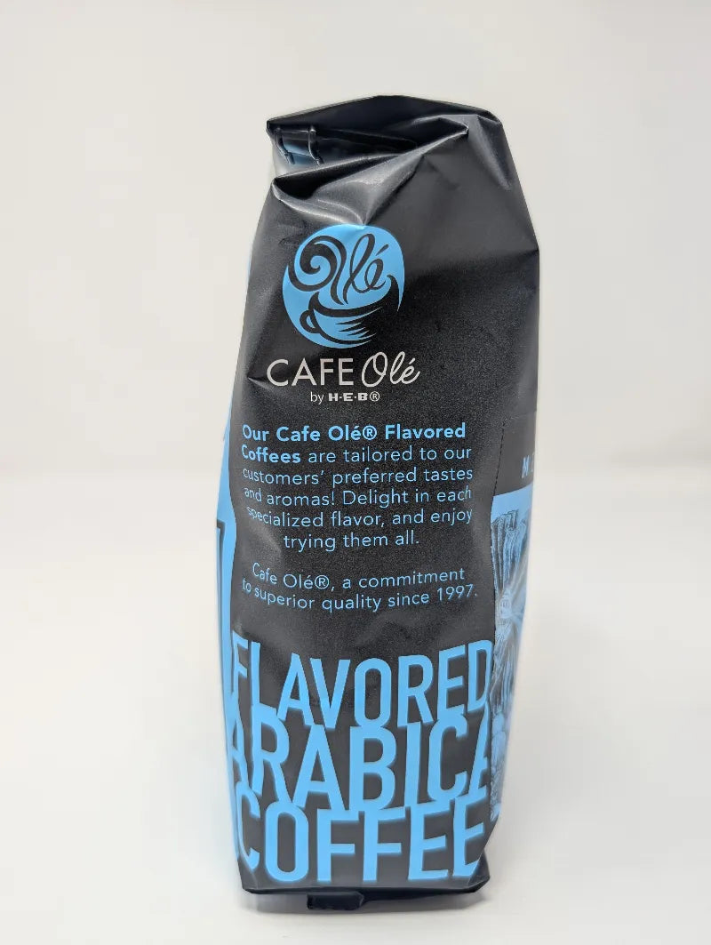 Side view of a dark gray and blue 12 ounce bag of Cafe Ole Cinnamon Hazelnut whole bean coffee on a white background.