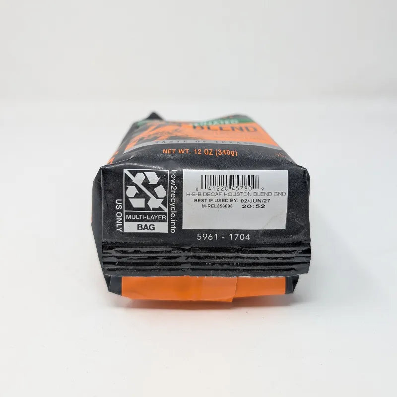 Bottom view of a 12 ounce bag of Cafe Ole by HEB Houston Blend Decaffeinated Ground Coffee. It features an orange and black color scheme with an image of the space shuttle on a white background.