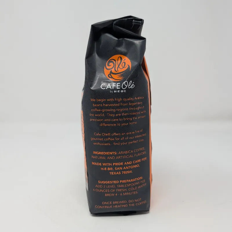Side view of a 12 ounce bag of Cafe Ole by H-E-B Rio Grande Especial ground coffee featuring the ingredients list and an orange and black color scheme on a plain white background.