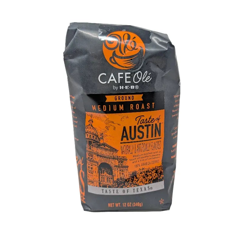 Front view of a 12 ounce bag of Cafe Olé by H-E-B Ground Medium Roast Taste of Austin coffee, featuring a black and orange package design with an illustration of the Texas state Capitol.