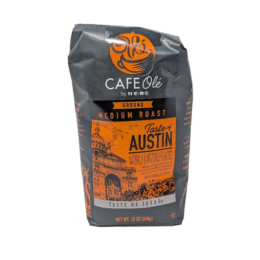 Front view of a 12 ounce bag of Cafe Olé by H-E-B Ground Medium Roast Taste of Austin coffee, featuring a black and orange package design with an illustration of the Texas state Capitol.