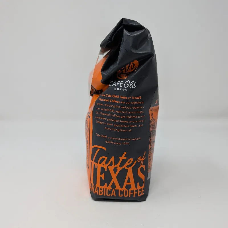 Side view of a 12 ounce bag of Cafe Olé by H-E-B Ground Medium Roast Taste of Austin coffee, featuring a black and orange package design.