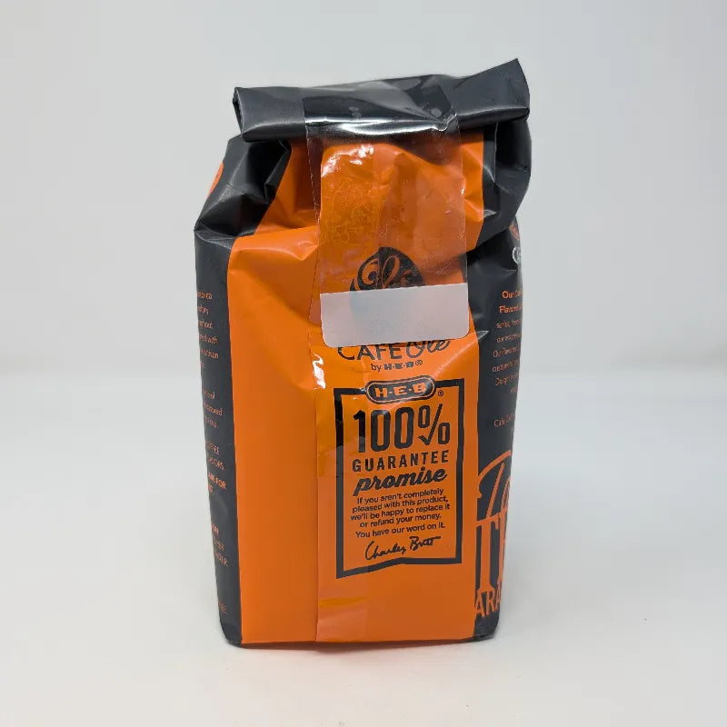 Rear view of a 12 ounce bag of Cafe Olé by H-E-B Ground Medium Roast Taste of Austin coffee, featuring a black and orange package design.