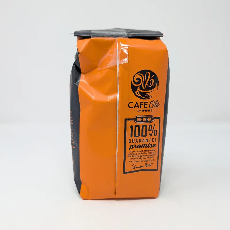 Rear view of a 12 ounce bag of Cafe Ole by H-E-B Taste of DFW Medium Roast Ground Coffee featuring an orange and black color scheme on a plain white background.