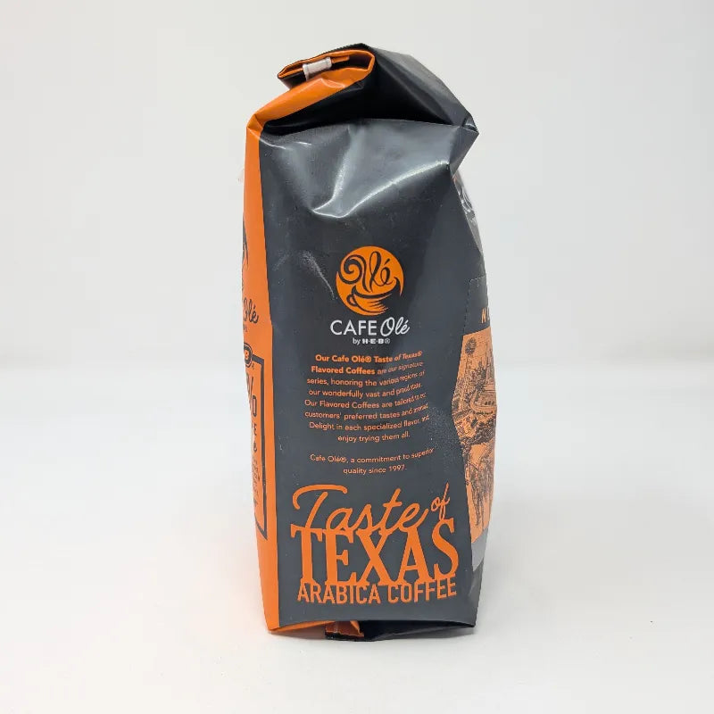Side view of a 12 ounce bag of Cafe Ole by H-E-B Taste of DFW Medium Roast Ground Coffee featuring an orange and black color scheme on a plain white background.