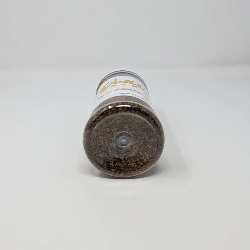 Bottom view of a clear plastic spice jar filled with dark brown all-purpose rub, featuring a white label with gold lettering that reads 'Goldee's Bar-B-Q' and 'ALL-PURPOSE RUB'. The jar has a white plastic lid and is photographed on a solid white background.