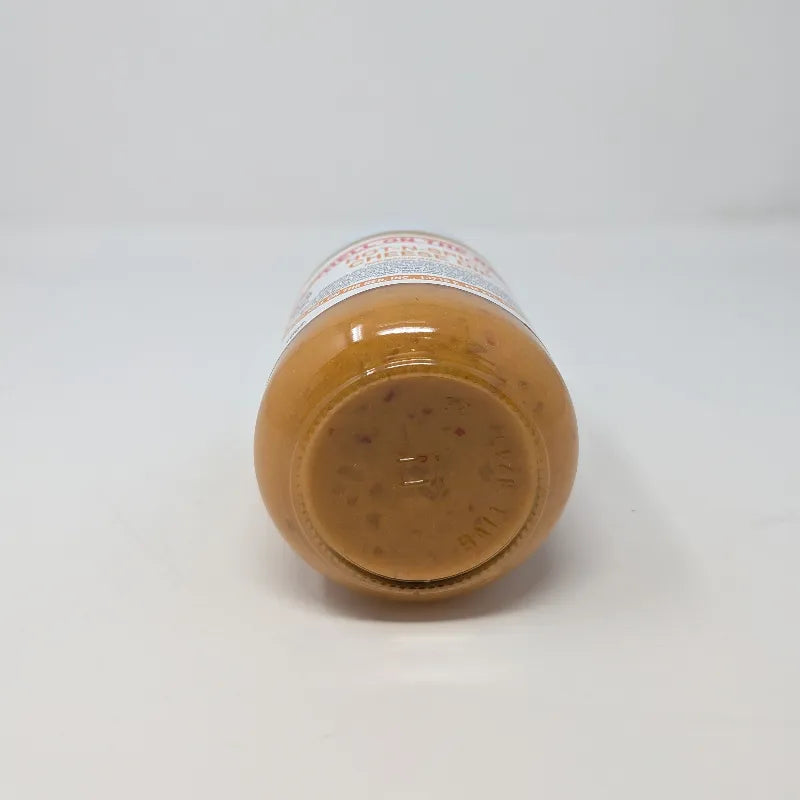 Bottom view of a jar of Hell on the Red Cheese Dip with a white label featuring yellow text and containing yellow queso on a white background.