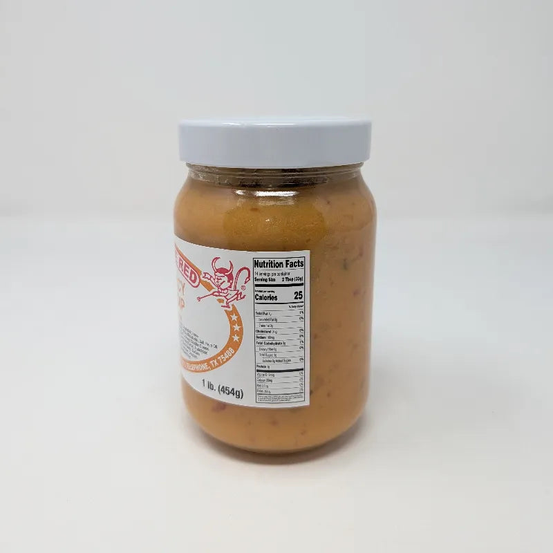 A jar of Hell on the Red Cheese Dip with a white label featuring yellow text and Nutrition Facts and containing yellow queso on a white background.