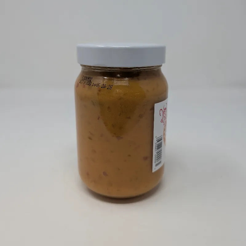 Side view of a jar of Hell on the Red Cheese Dip with a white label featuring yellow text and containing yellow queso on a white background.