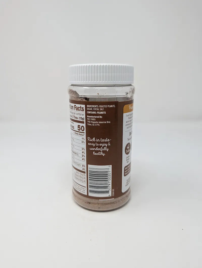 Side view of jar of PB2 Cocoa Peanut Powder on a plain white background. The product is in a clear plastic jar showing the brown powder inside, with a white ribbed lid and a brown and white label featuring the PB2 logo and cocoa bean illustrations.