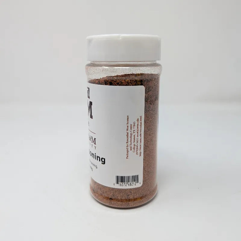 Side view of a clear plastic bottle of Texas A&M University Steak Seasoning with a white cap and white label, containing brown seasoning powder, on a white background.