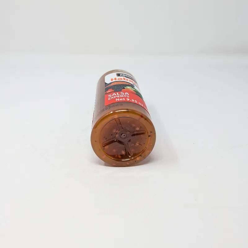 Bottom view of a bottle of Zaaschila Habanero Homestyle Hot Sauce on a plain white background. The bottle has a white cap with a built-in  loop, and features a label with red, white, and black colors showing peppers and a bowl of sauce.